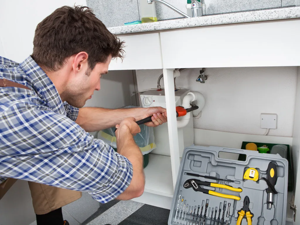 Plumber repairing a burst pipe under a sink in Mansfield