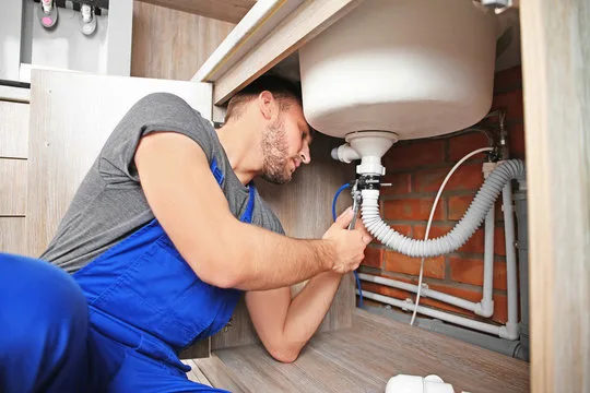 Plumber tightening a flexible waste pipe under a kitchen sink